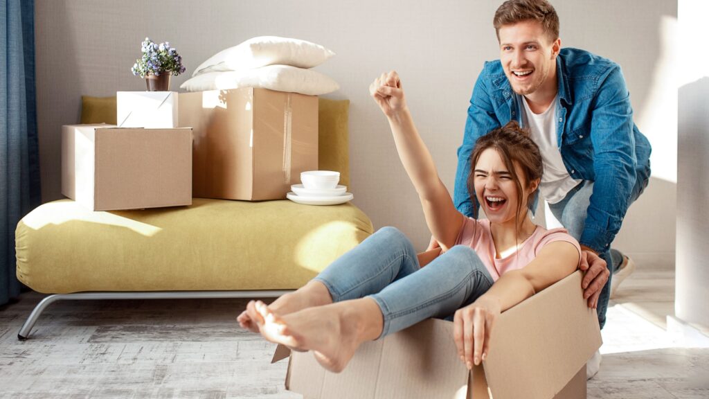 Happy young couple moving into their new home, surrounded by boxes, celebrating their first property purchase.